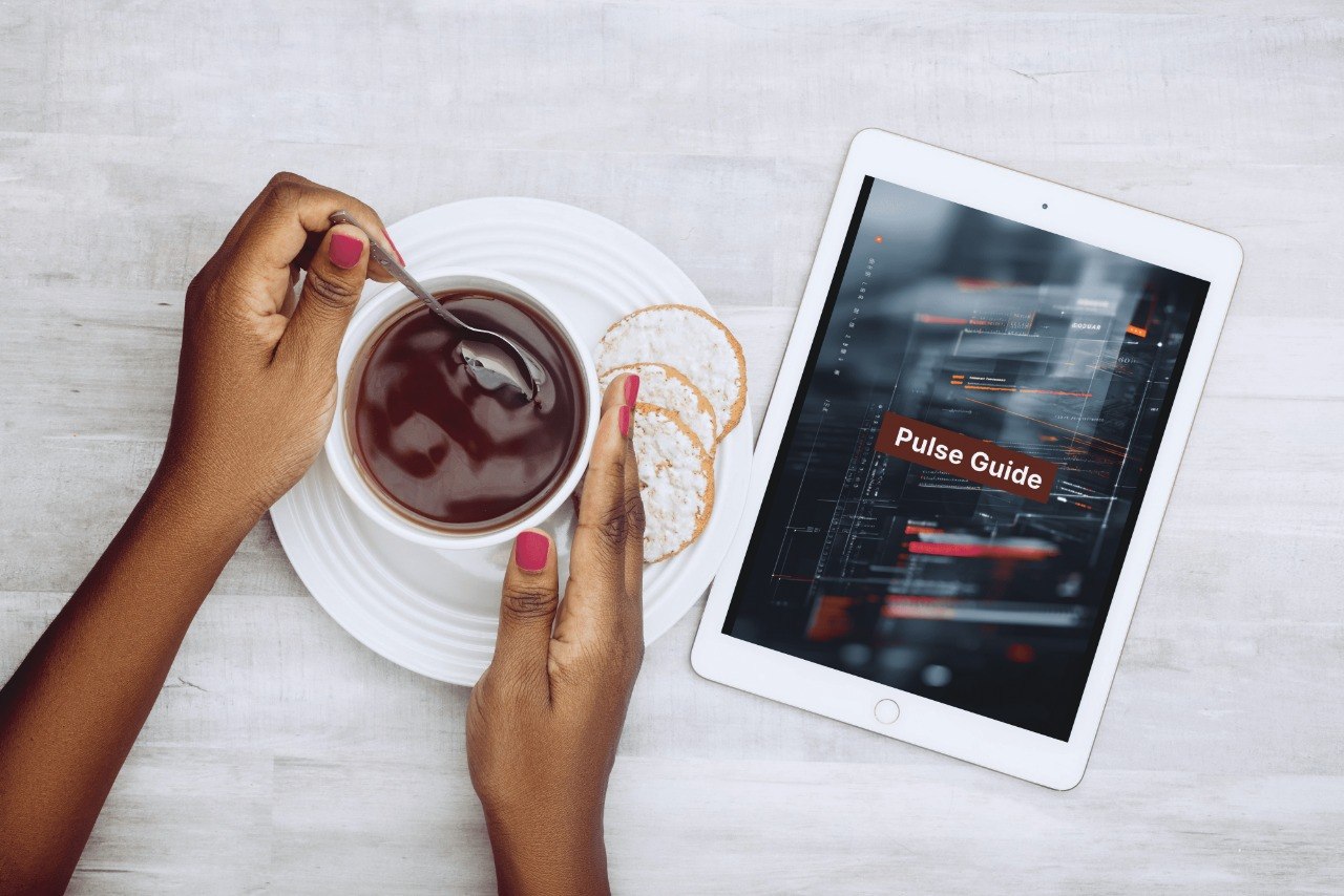 Person holding a cup of coffee with a tablet displaying a 'Pulse Guide' on a light surface.